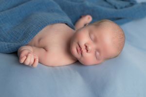 Peaceful sleeping newborn on light blue background with gentle natural lighting.