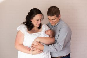 A tender family moment as parents hold and gaze at their newborn baby against a neutral backdrop.