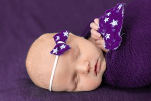 Sleeping newborn with purple star-patterned butterfly accessories on a purple background.
