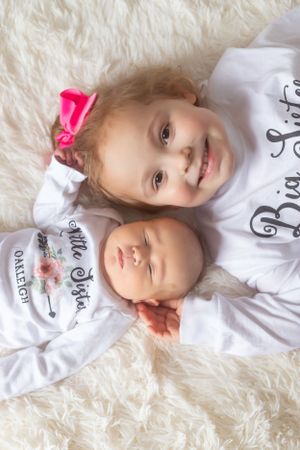Two children in white outfits laying on a fluffy white rug.