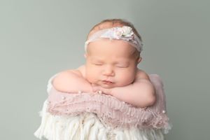 Sleeping newborn with delicate headband resting in a cream-colored basket.