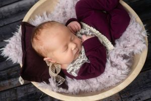 Sleeping baby in burgundy outfit on plush bedding in wooden bowl.