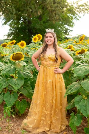Yellow ball gown and tiara creates fairy tale moment in sunflower field.
