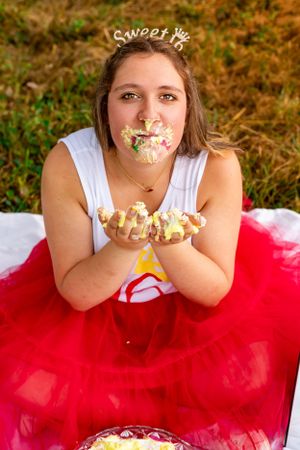 Playful cake smash photo featuring someone in a red tulle skirt with frosting on their face.
