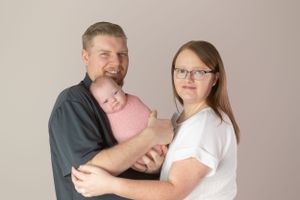 Family portrait showing three people in casual attire against a neutral studio background.