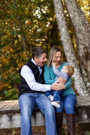 Family shares joyful moment together sitting on wooden bench in autumn forest.