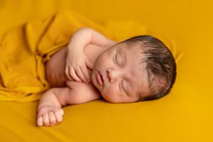 Sleeping newborn lies peacefully on golden yellow backdrop in natural pose.