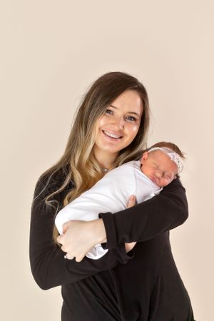 Portrait of woman in black holding sleeping baby against neutral background.