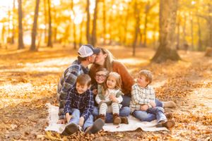 Family group sits together on fallen leaves during golden autumn afternoon.