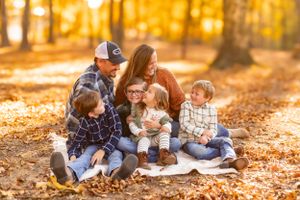 Family sits together on blanket during golden autumn afternoon in the woods.