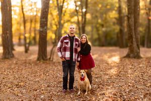 Couple poses with their dog on fallen leaves in autumn forest.