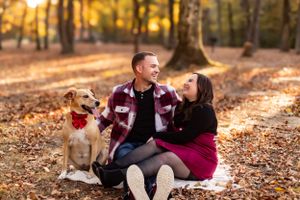 Couple laughs with their dog while sitting on blanket in autumn woods.