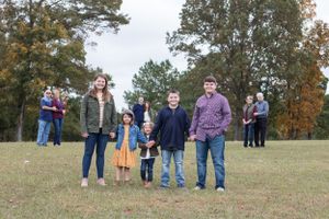 Group poses together on a grassy hill during fall with autumn trees in the background.