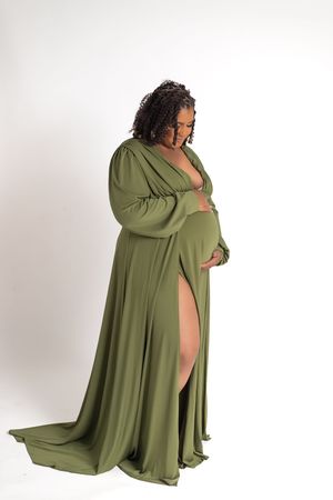Person wearing a flowing olive green maxi dress with long sleeves and dramatic side slit poses against white background.