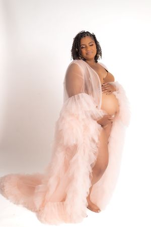 Artistic maternity portrait with figure wearing flowing peach tulle robe against white background.