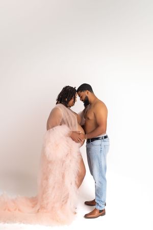 An intimate maternity photo featuring a flowing peach tulle dress against a white backdrop.
