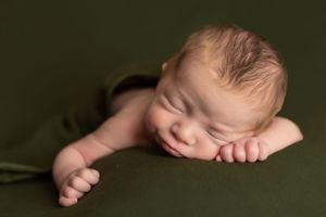Sleeping newborn resting on green fabric in artistic portrait style.