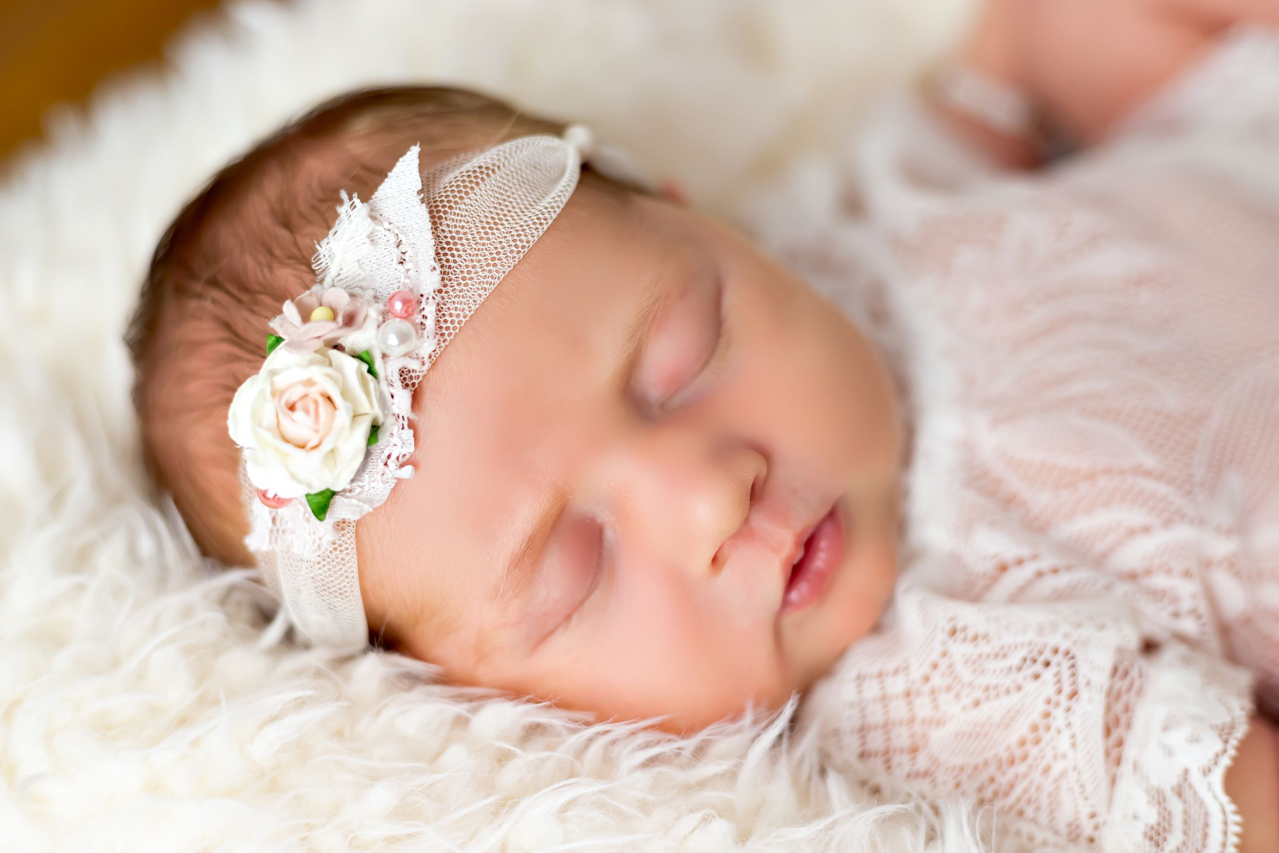 Sleeping baby with delicate floral headband on white lace blanket.