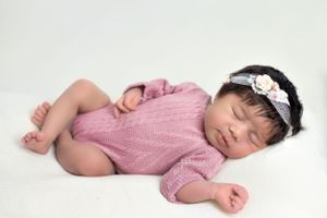 Sleeping baby in pink knit romper with white lace headband.