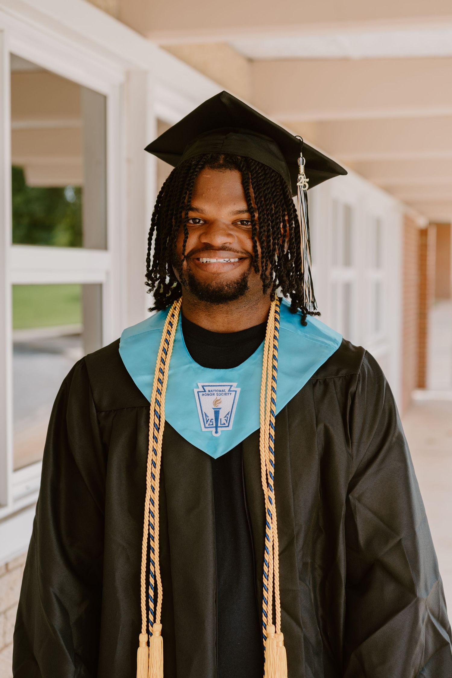 Graduate in black cap and gown with gold honor cords smiles during graduation ceremony.