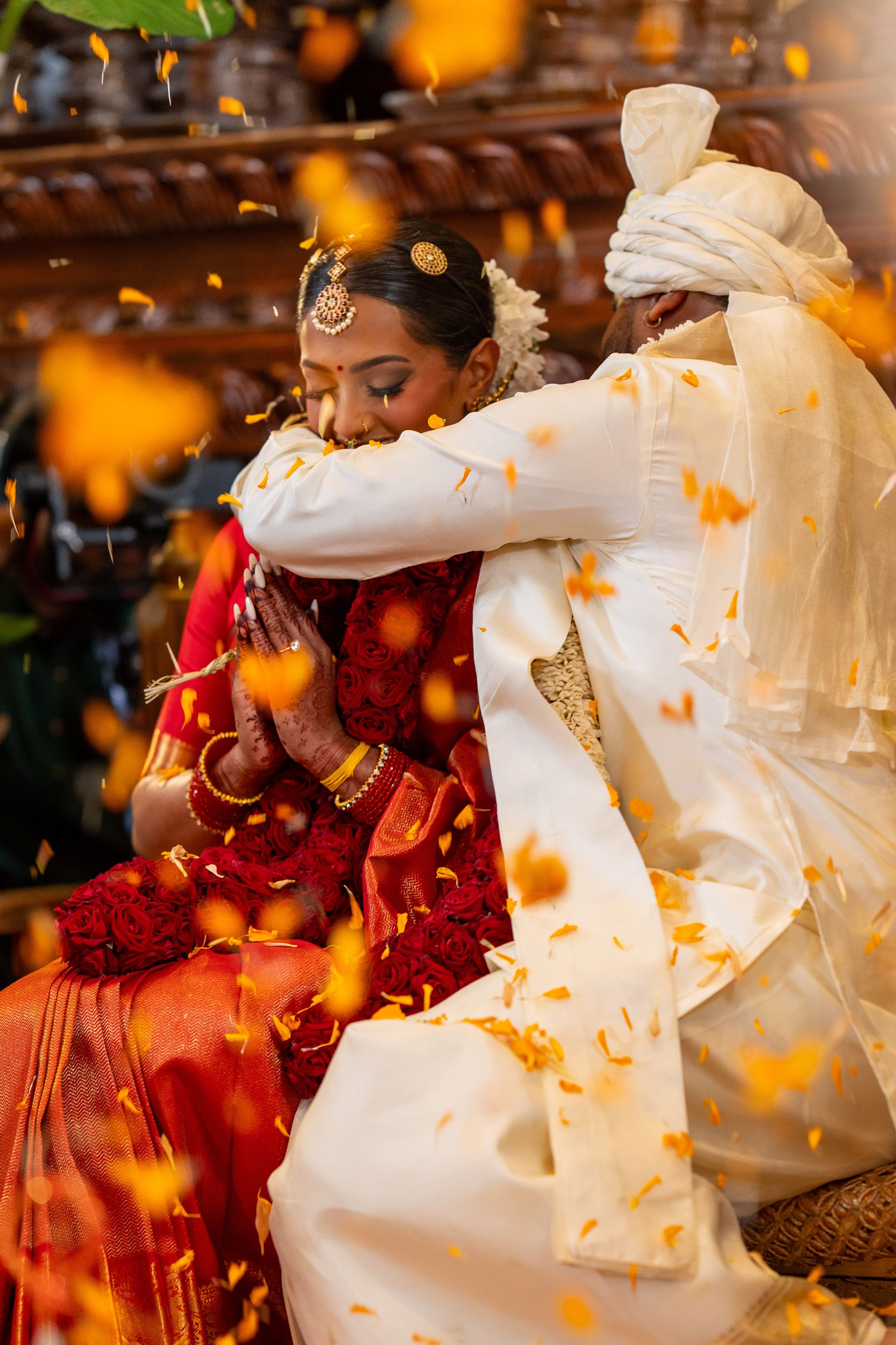 Orange flower petals fall around a traditional Indian wedding ceremony with red and white attire.