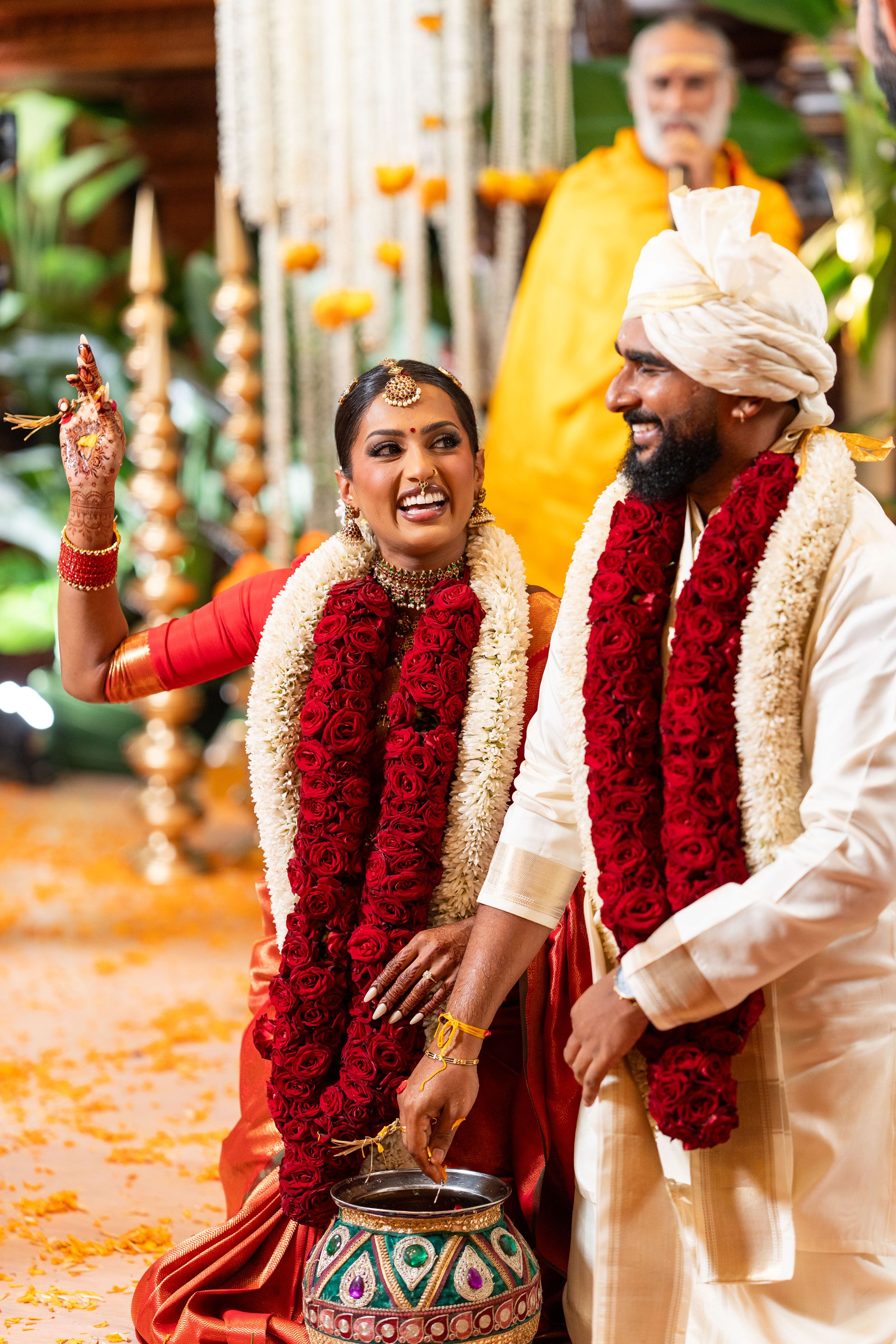 A couple in traditional Indian wedding attire with red garlands share a joyful moment during their wedding ceremony.