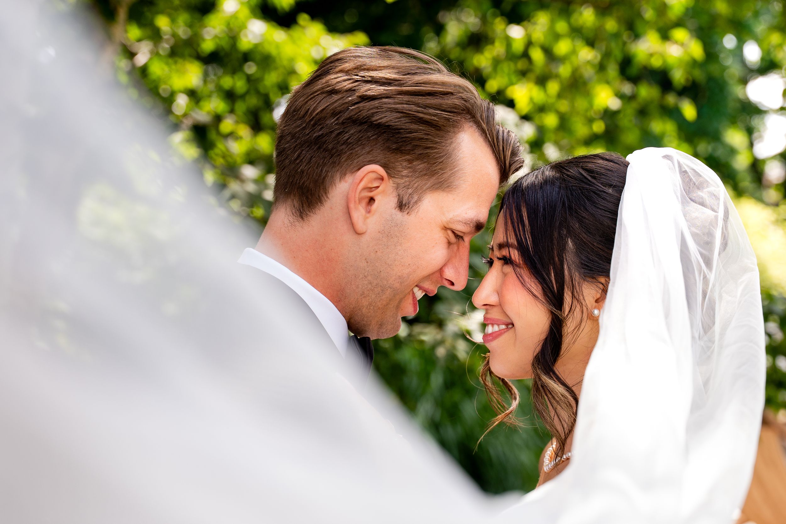 Intimate wedding portraits captured in a bright garden setting with natural lighting, the couples faces are framed by the bride's veil.