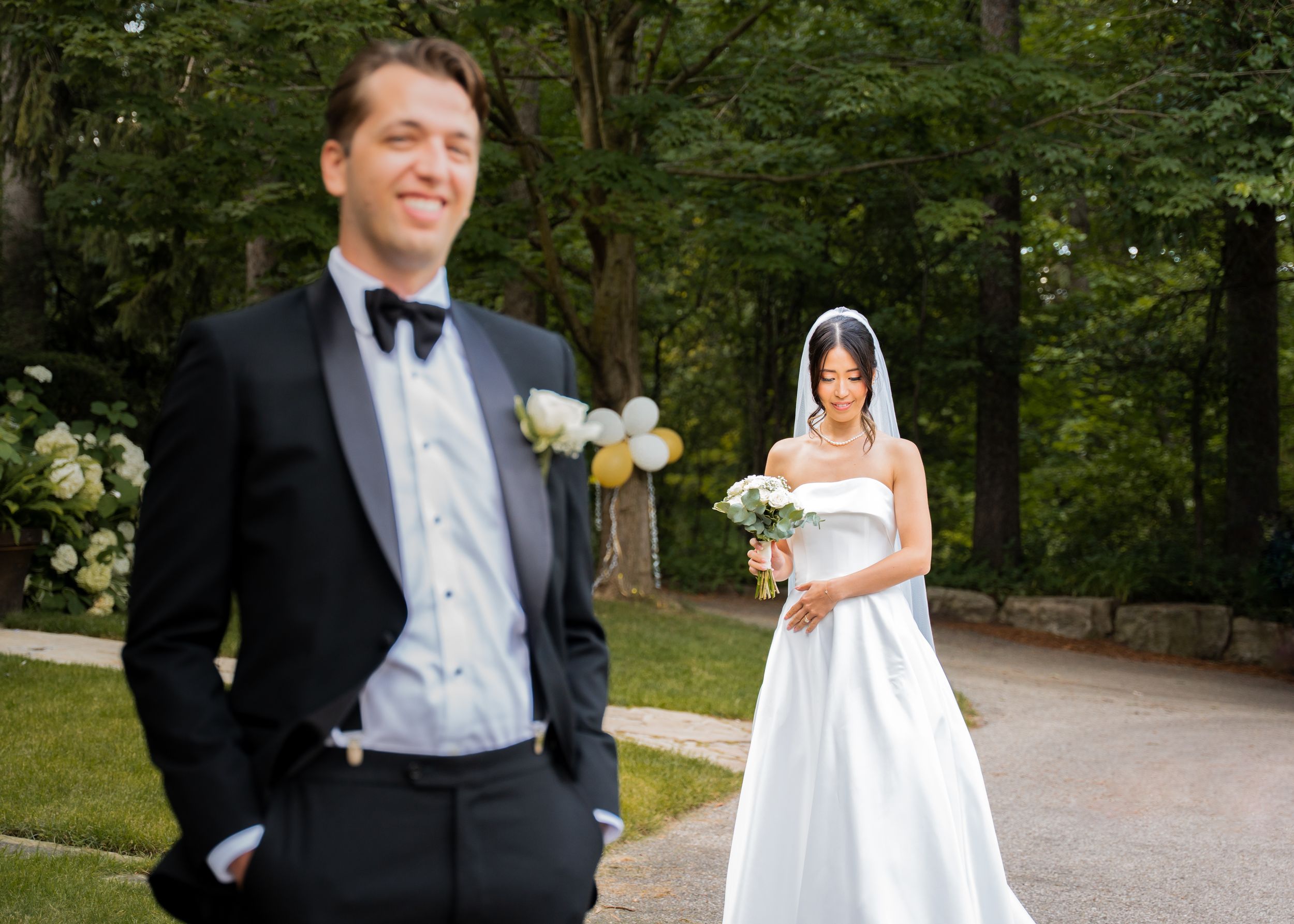 A bride walks up to her fiancé for a first look in her wedding gown. The groom is smiling in anticipation of seeing his bride.