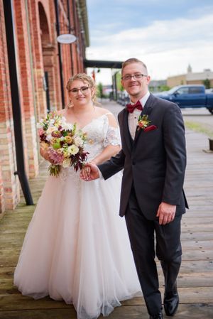 A romantic outdoor wedding portrait with rustic brick architecture in the background.
