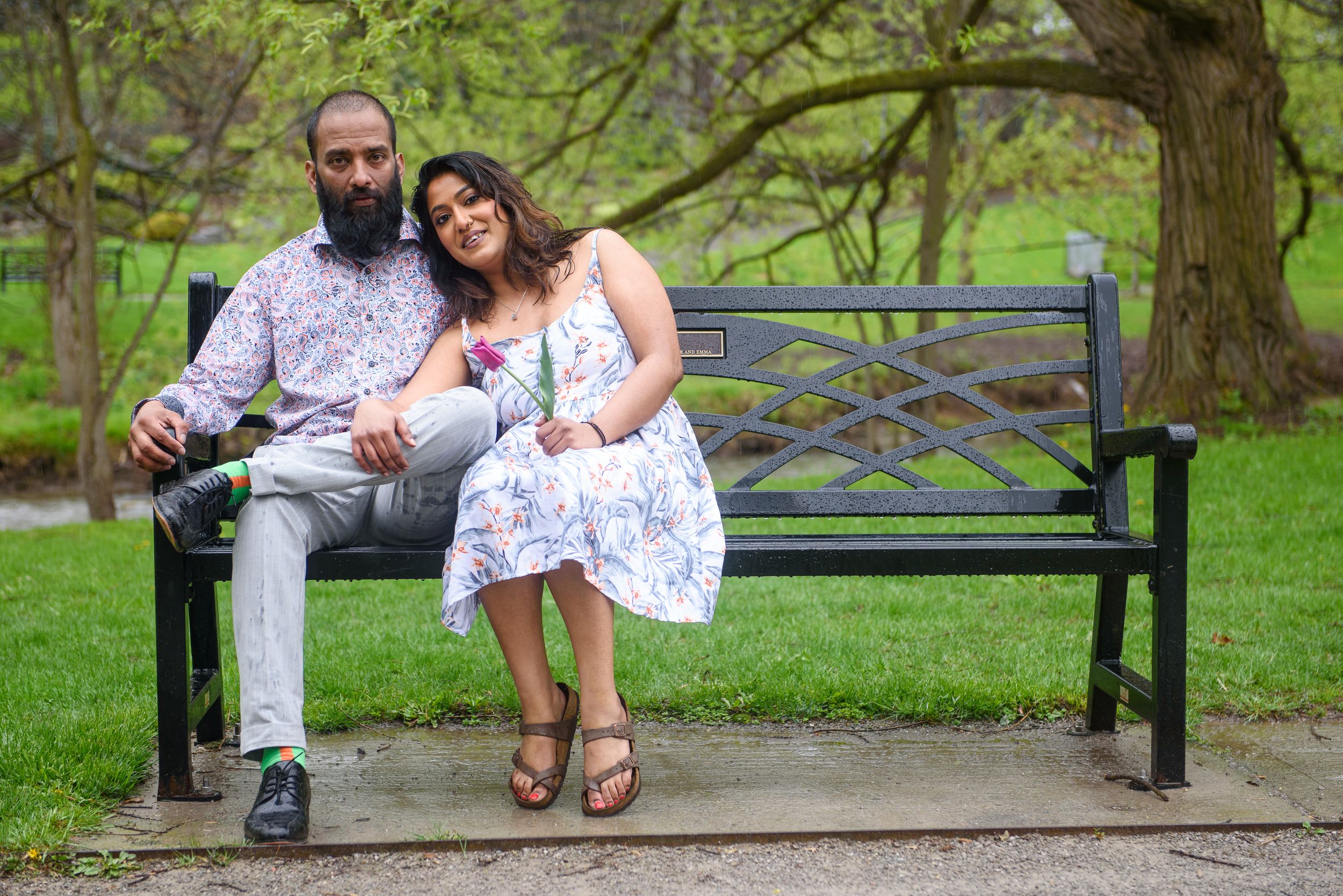 A couple relaxes together on a park bench surrounded by lush spring greenery.