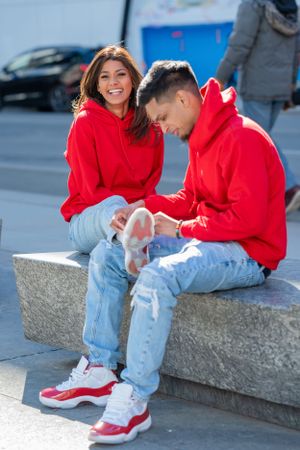 Casual couple in matching red hoodies and jeans sitting on concrete steps outdoors.