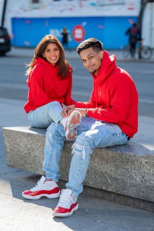 Playful couple in matching red hoodies share laughs while sitting on urban steps.