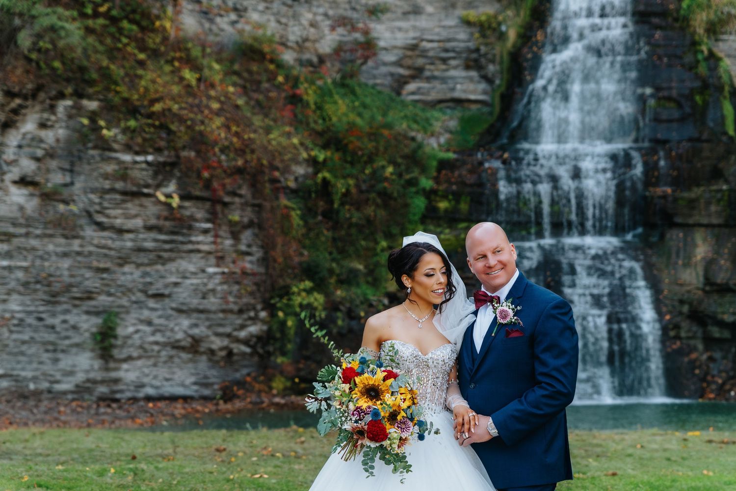 Newlyweds pose together in front of majestic waterfall.