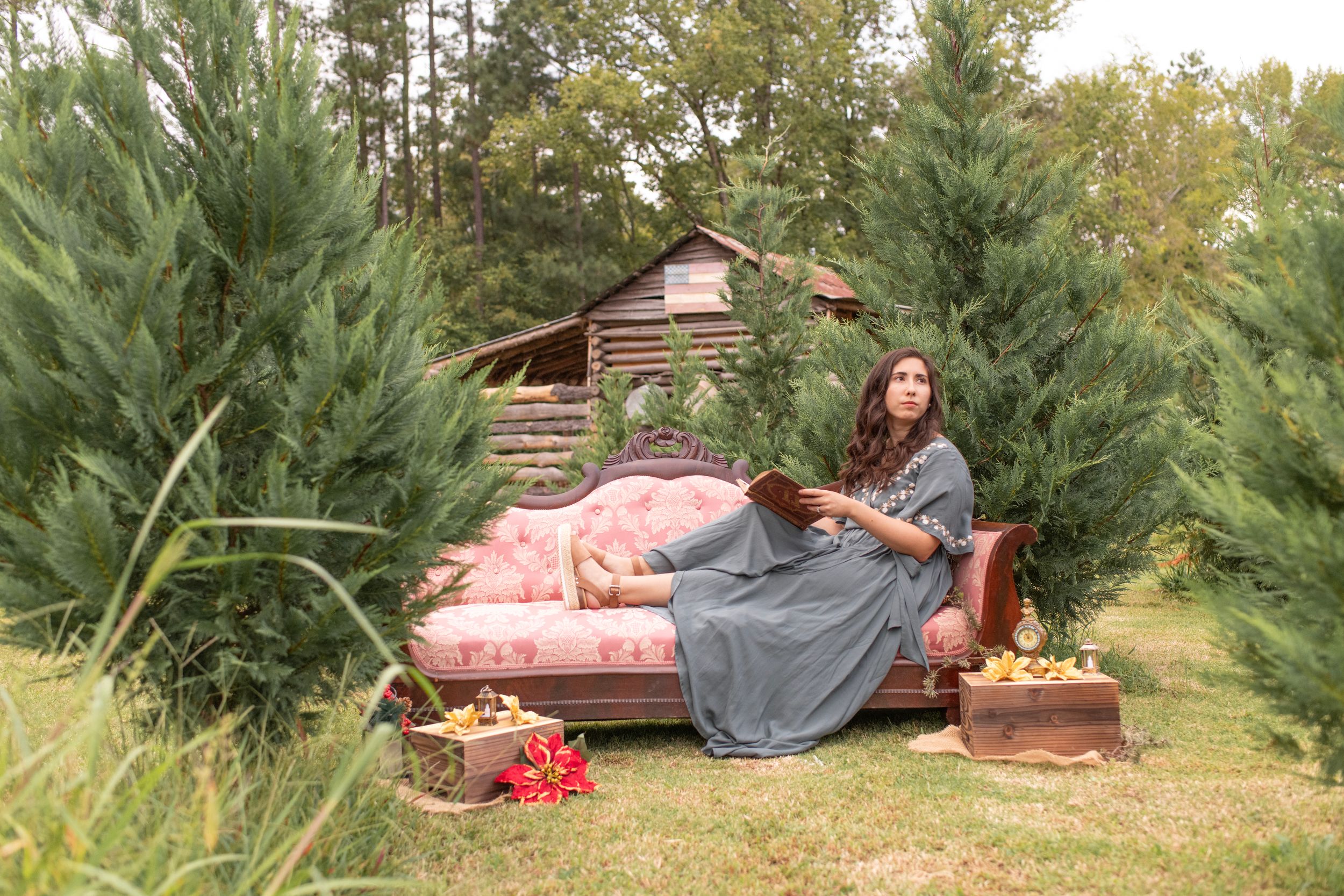 Vintage Christmas Mini Session at Lakewood Tree Farm in Chapin, SC. Girl poses with books and vintage couch in front of barn.