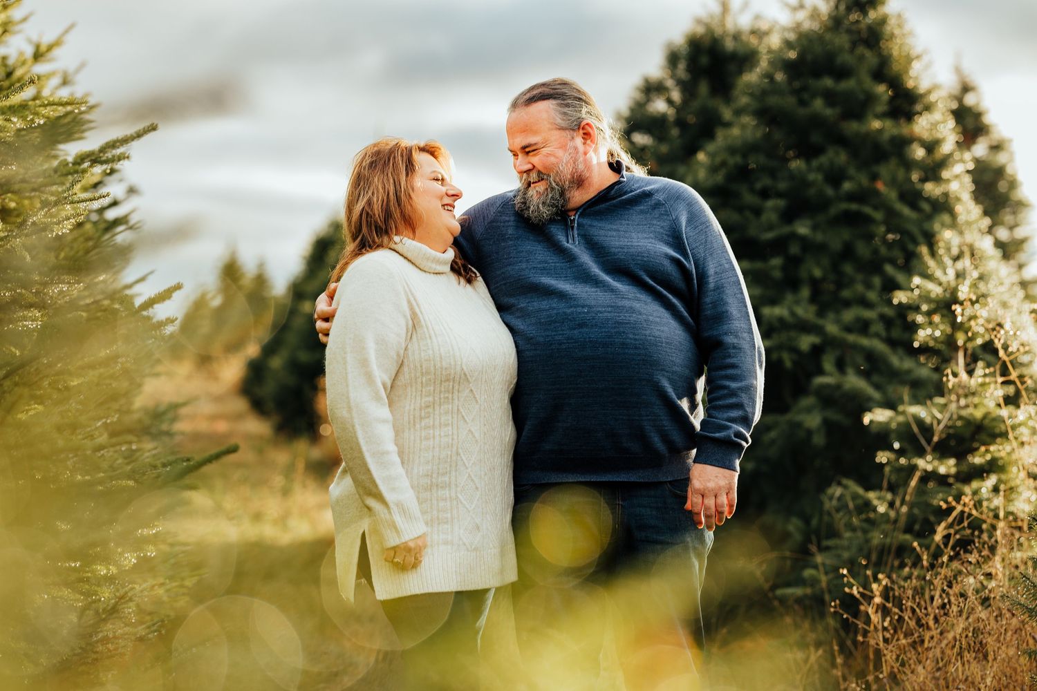 A husband and wife look at each other with big smiles during a family photo shoot at a Christmas Tree Farm in Walla Walla Washington