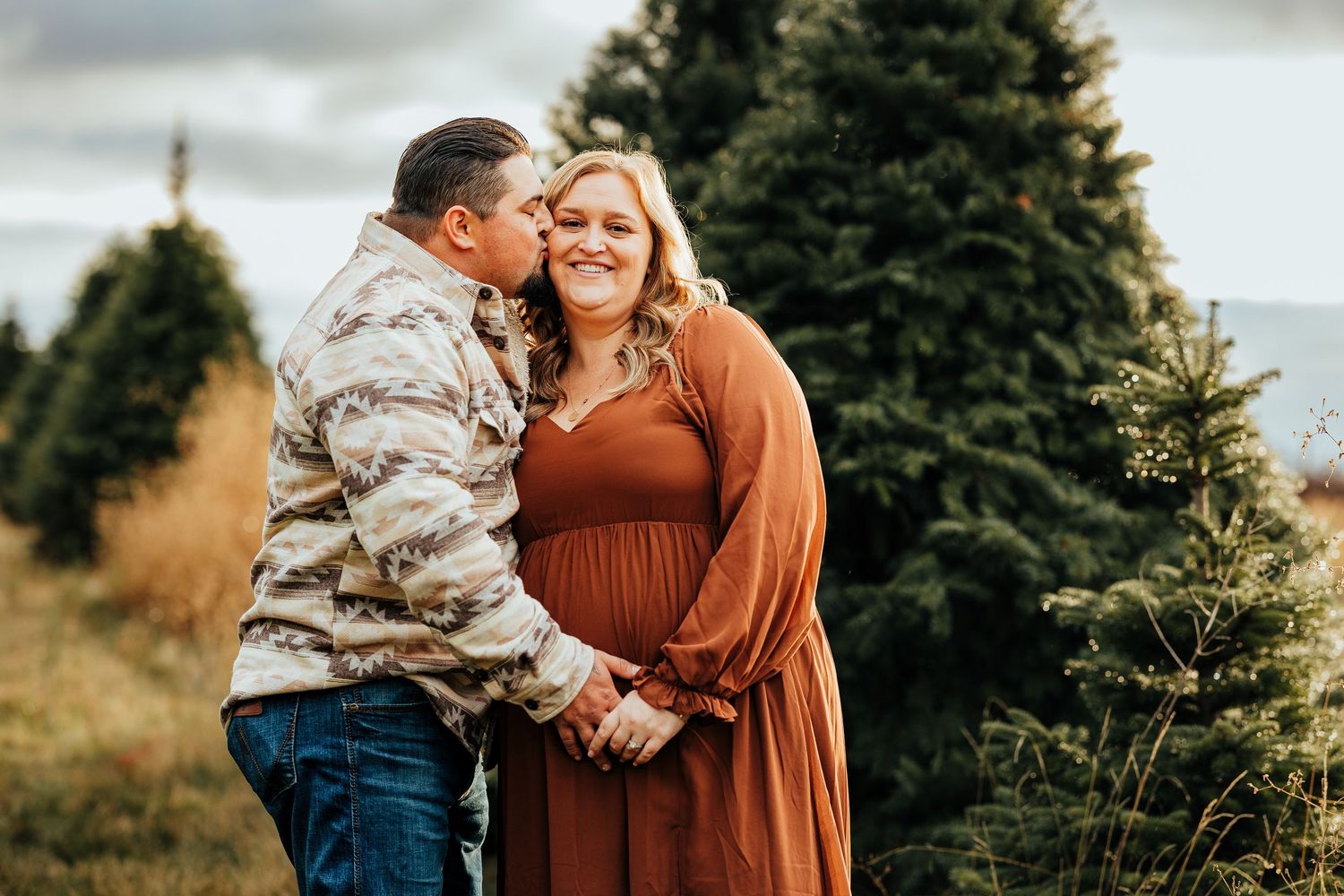 A husband kisses his pregnant wife's cheek during a christmas tree farm family photo shoot in Walla Walla Washington