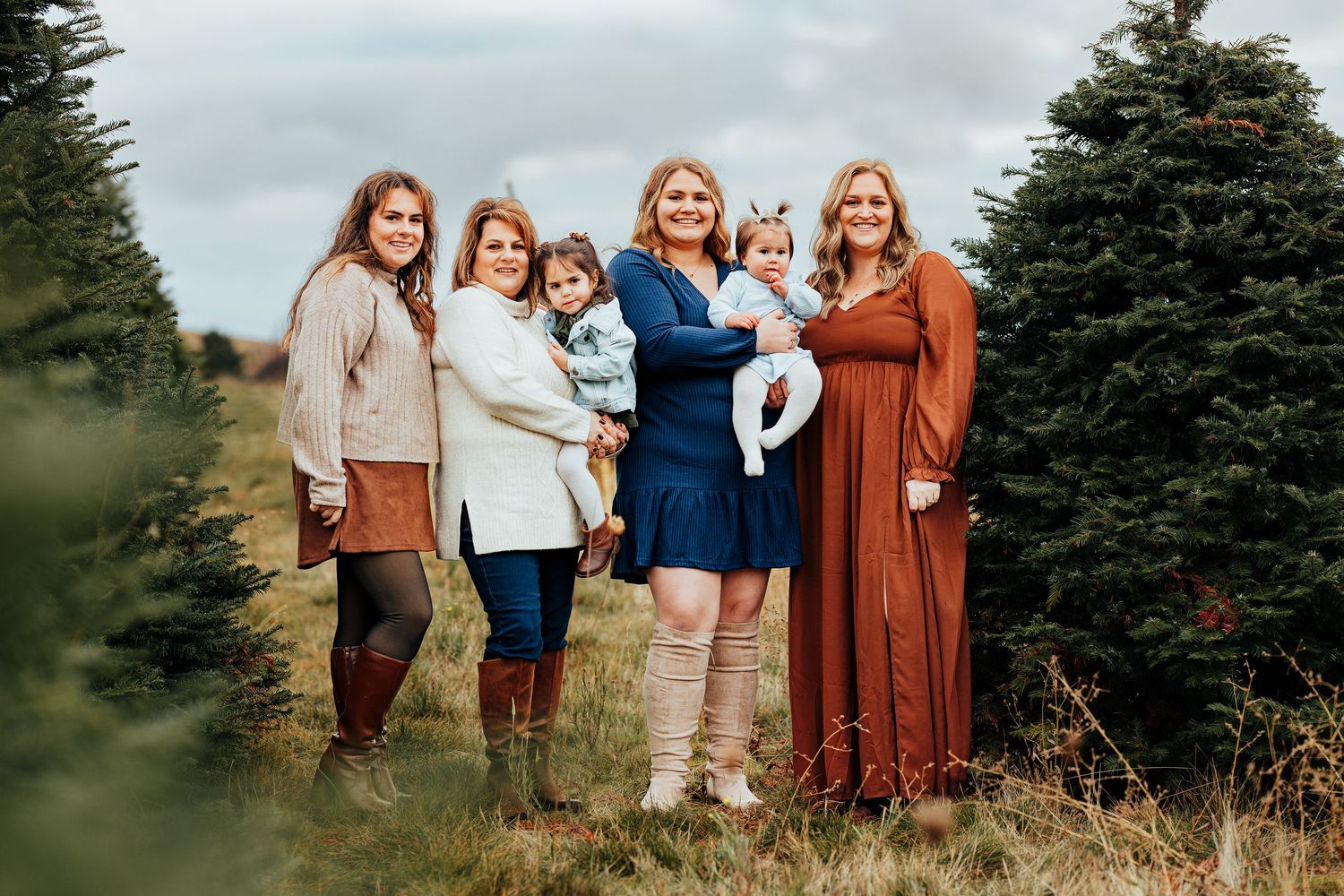 A family photo with all of the females posed looking at the camera during sunset at a christmas tree farm