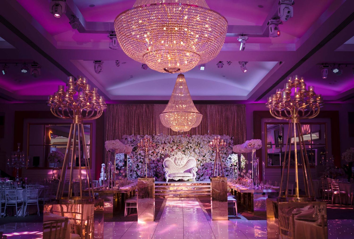 An opulent wedding reception venue with crystal chandeliers and purple lighting creating a luxurious atmosphere.