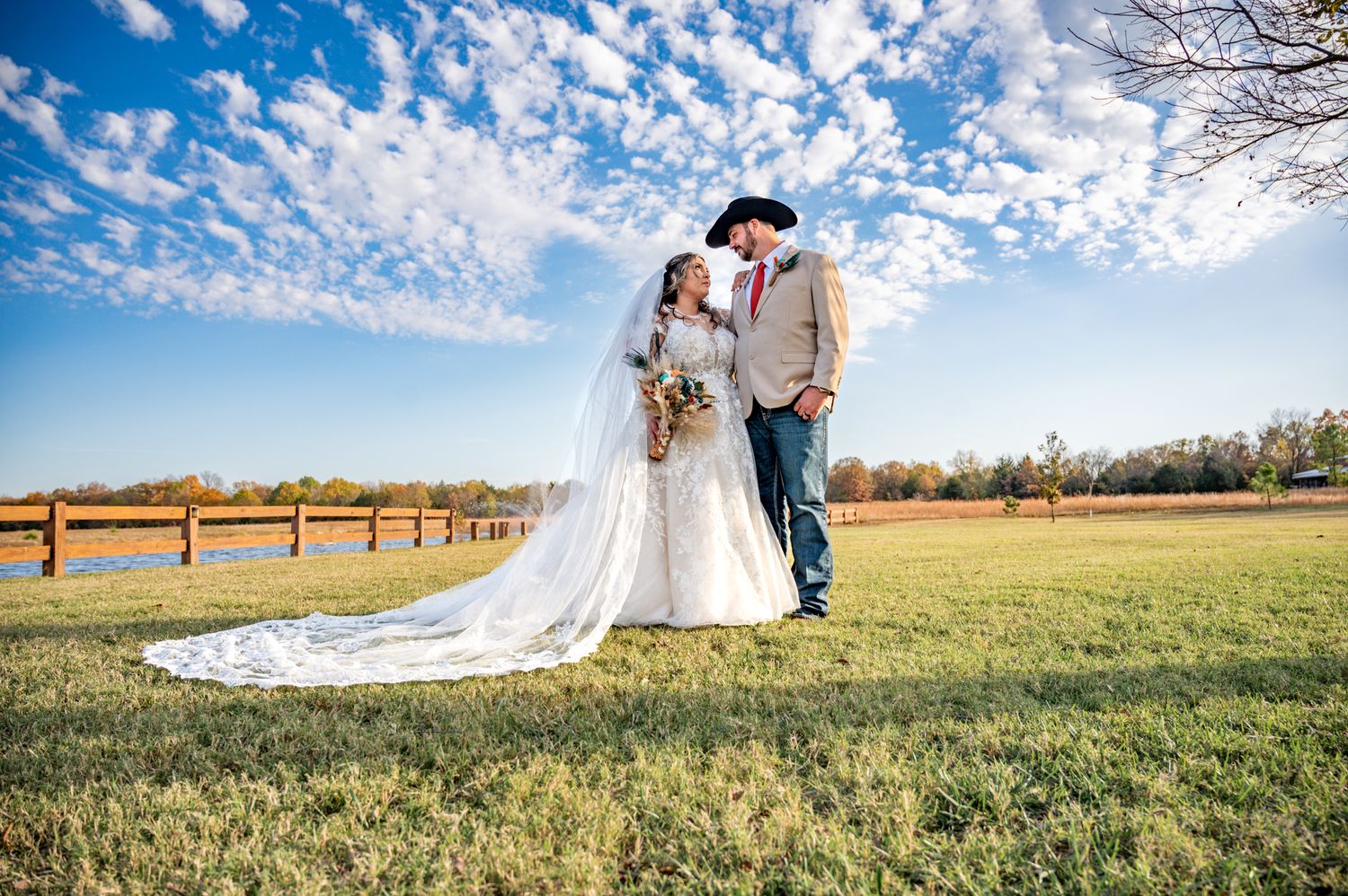 A couple poses together on their wedding day under a dramatic blue cloudy sky in an open field.