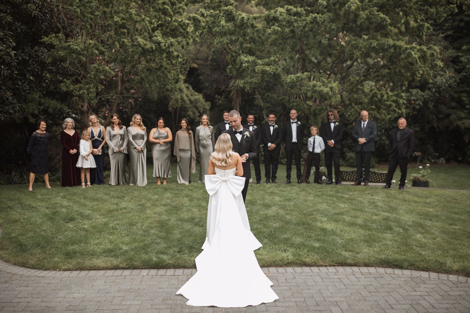 A wedding party lineup on a manicured lawn with the couple in the center.
