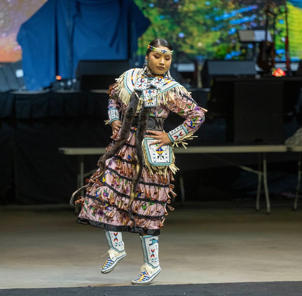 Dancer in a patterned dress performs a dynamic spinning movement on an outdoor stage during a performance.