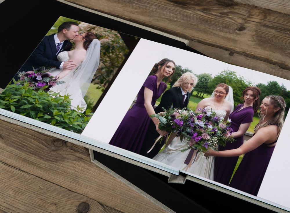 Wedding photo album showing ceremony and bridal party pictures on wooden table.
