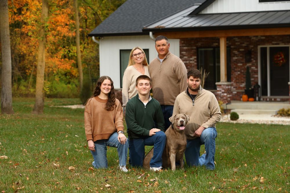 A group sits on grass with a golden retriever dog surrounded by vibrant fall foliage and autumn colors.