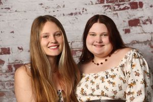 Two friends pose together against a rustic brick wall background in a studio portrait setting.