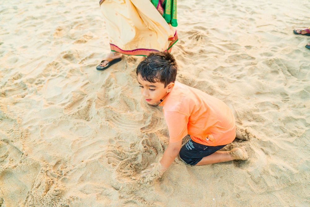Child in orange shirt playing in beach sand near green structure.