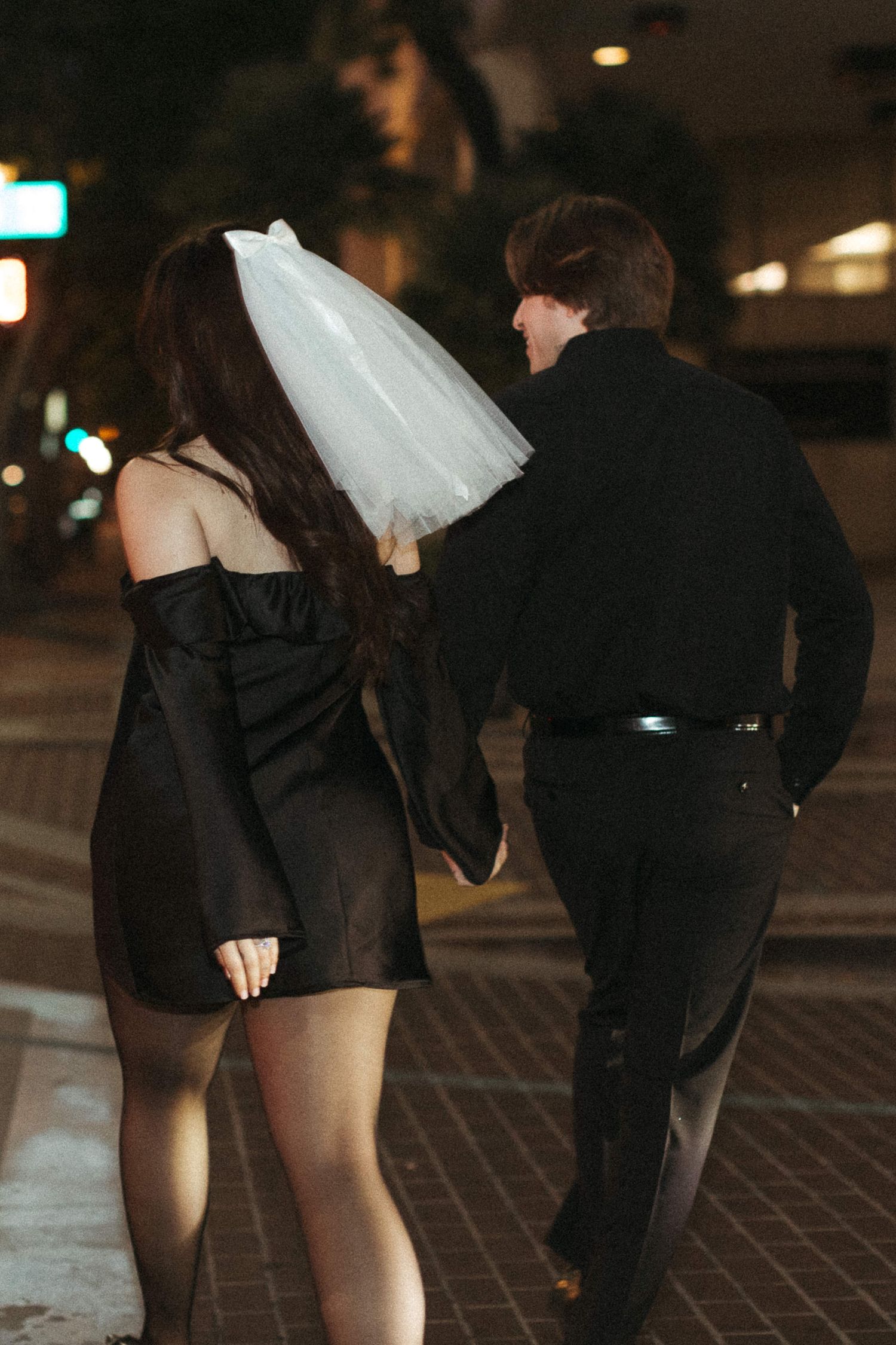 Couple walking at night with bridal veil flowing in urban setting.
