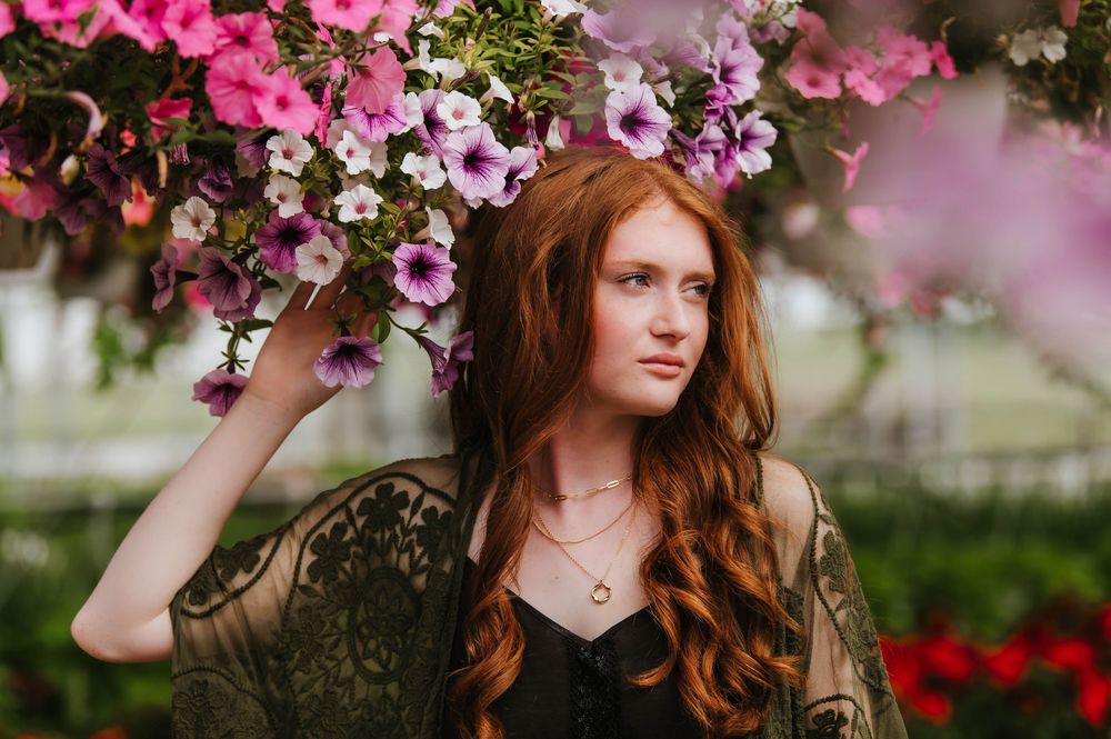 A person wearing a black dress stands beneath vibrant pink flowers in a spring garden setting.