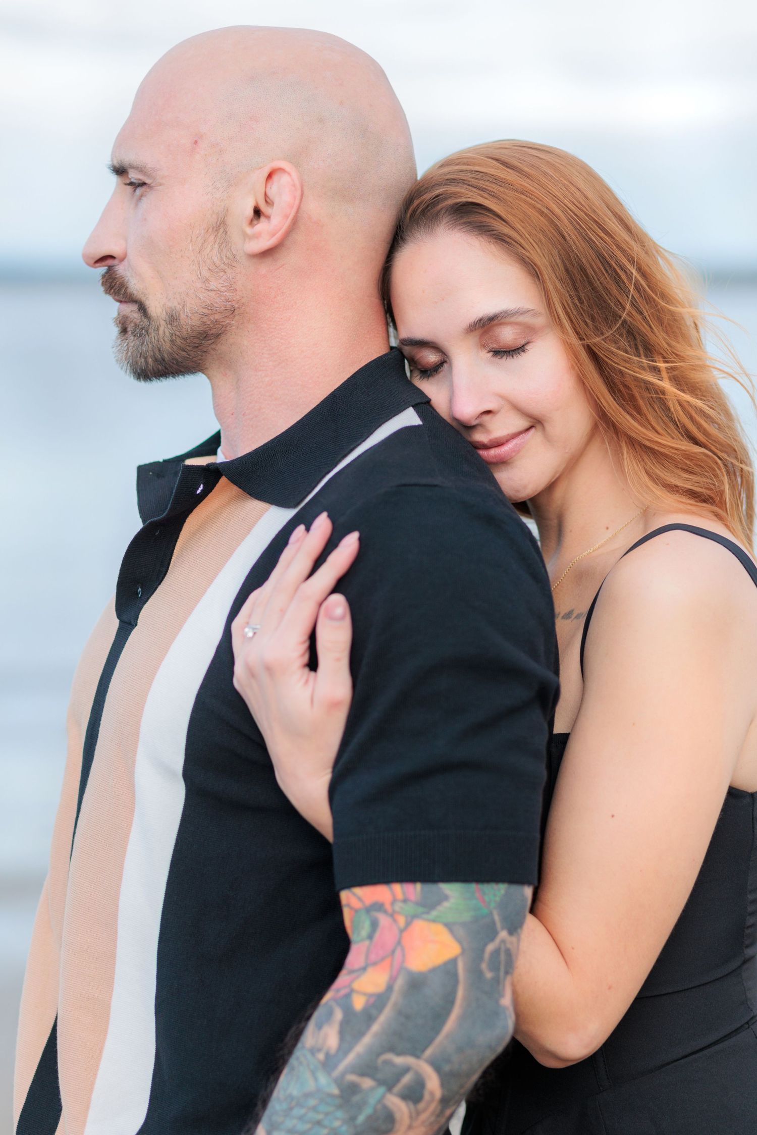 A couple in romantic embrace stands against a light background showing close physical connection and emotional intimacy.
