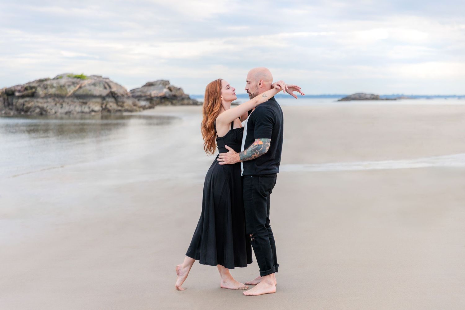 Couple dancing intimately together on a misty beach with rocky outcrops and mountains in the background.