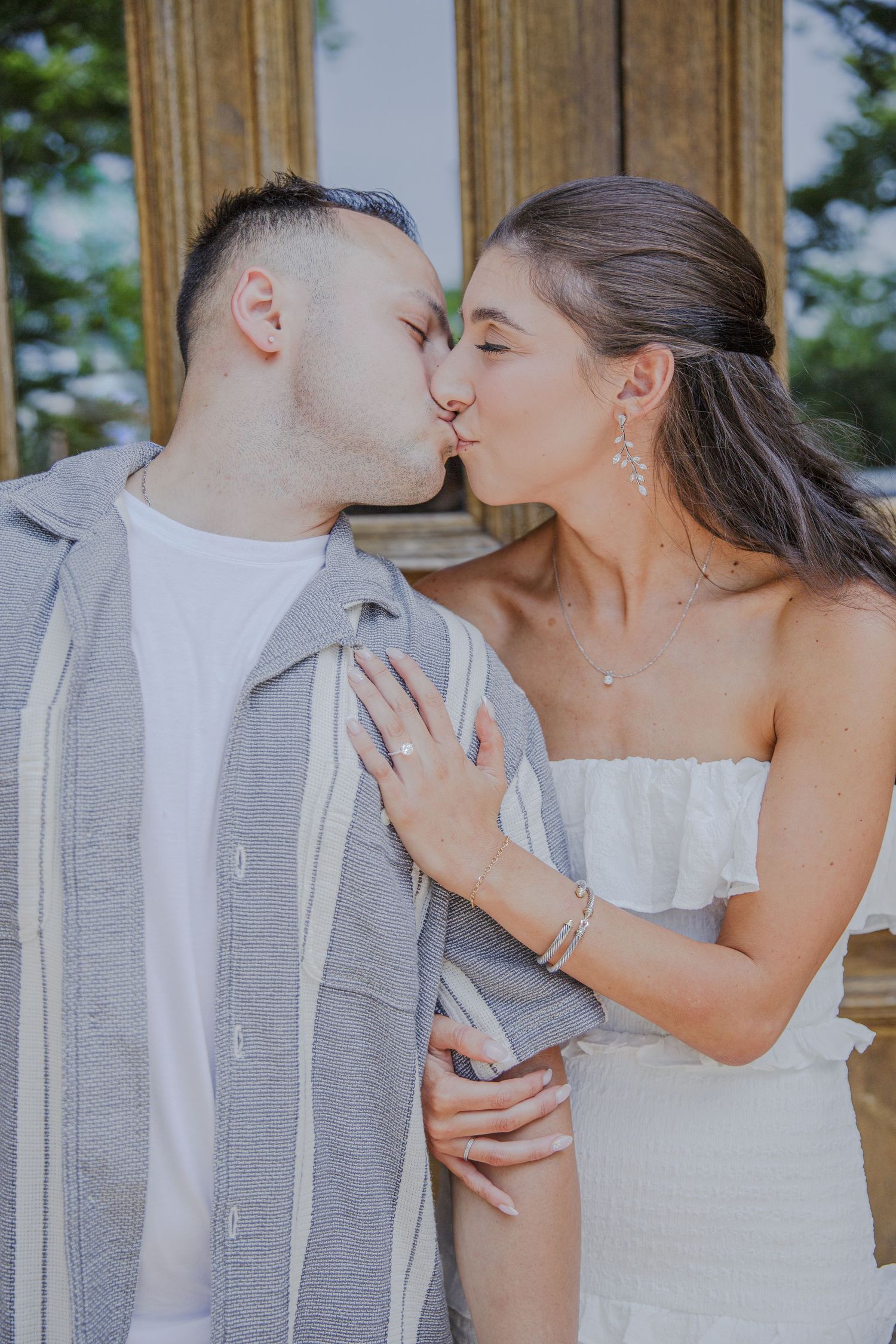 A romantic kiss between a couple in wedding attire, with the bride in white and groom in a gray button-up shirt.